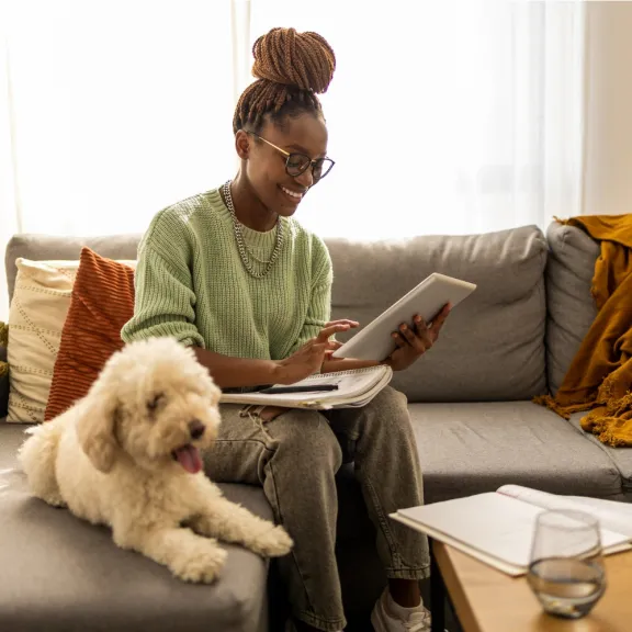 Woman sitting with her dog on a sofa using a tablet